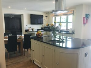 A kitchen with a central island, a dining area with chairs, a television mounted on the wall, and a window with a view. - Large detached property with a patio, hot tub and enclosed garden. (Llangammarch Wells, near Builth Wells)