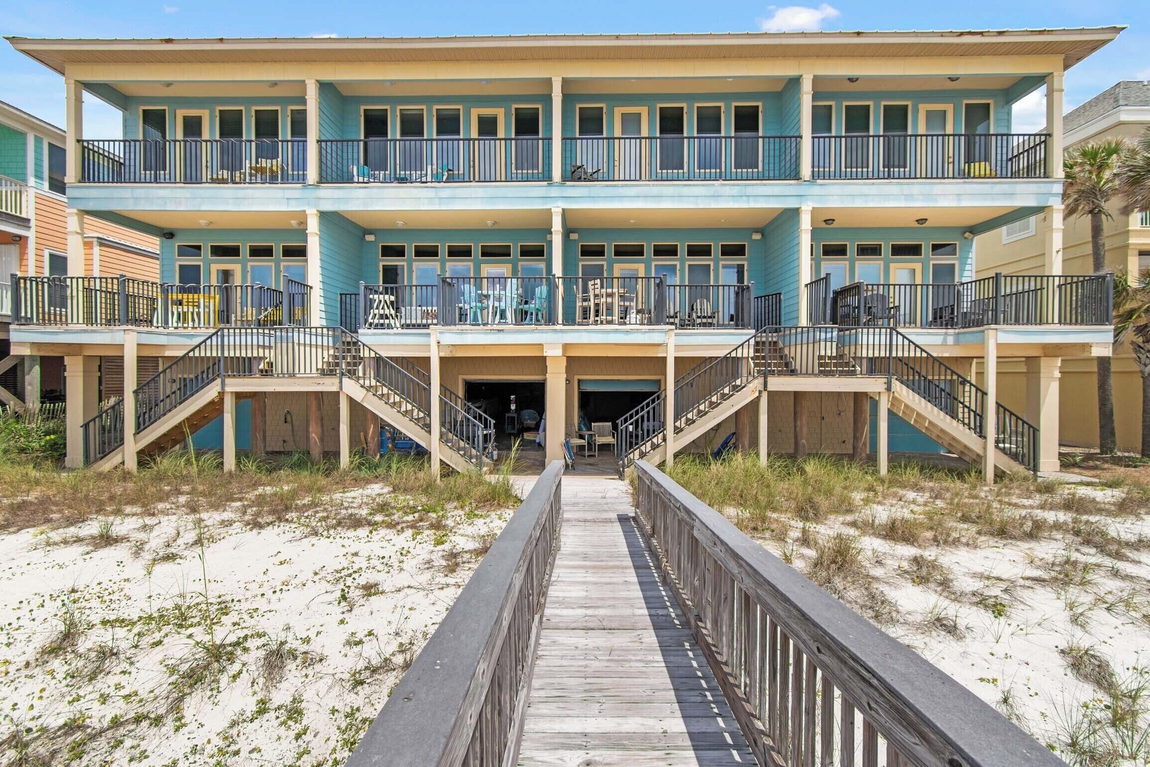 A multi-story beachfront hotel with a central entrance, balconies, and a wooden boardwalk leading to the entrance.