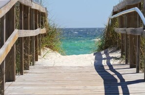 Un muelle de madera que conduce a una playa con aguas turquesas cristalinas y dunas arenosas.