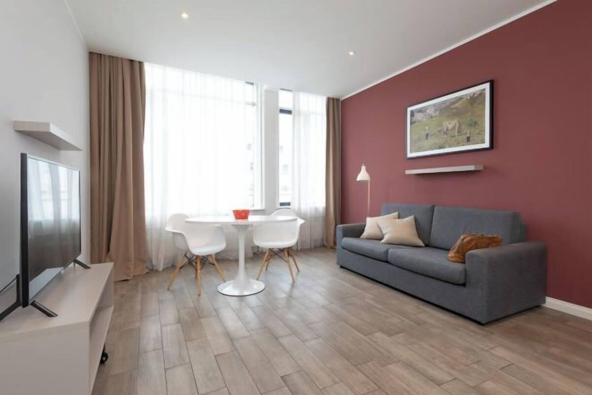 Un salon moderne avec un canapé gris, une table blanche et un téléviseur.