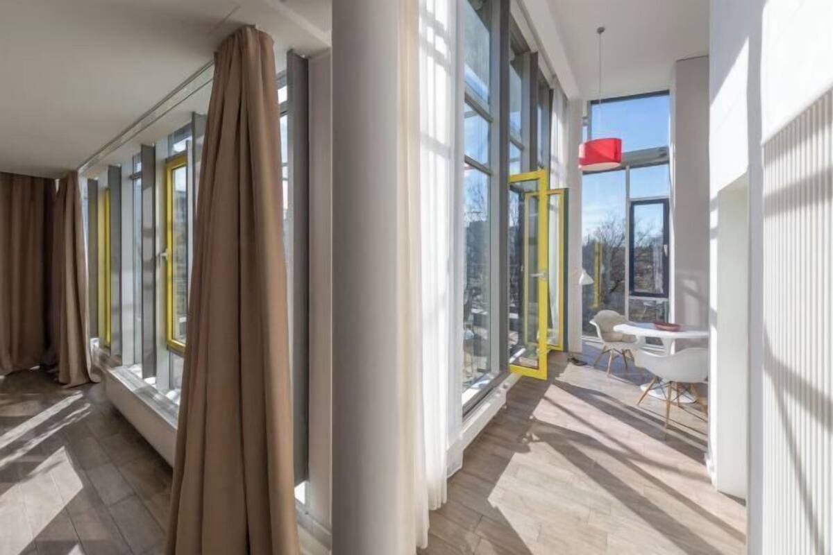 Un intérieur d’hôtel moderne avec de grandes fenêtres, une colonne centrale et un espace salon agrémenté d’une touche de rouge.