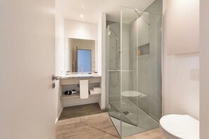 Un baño moderno con cabina de ducha de vidrio, inodoro blanco y lavamanos con espejo sobre él.