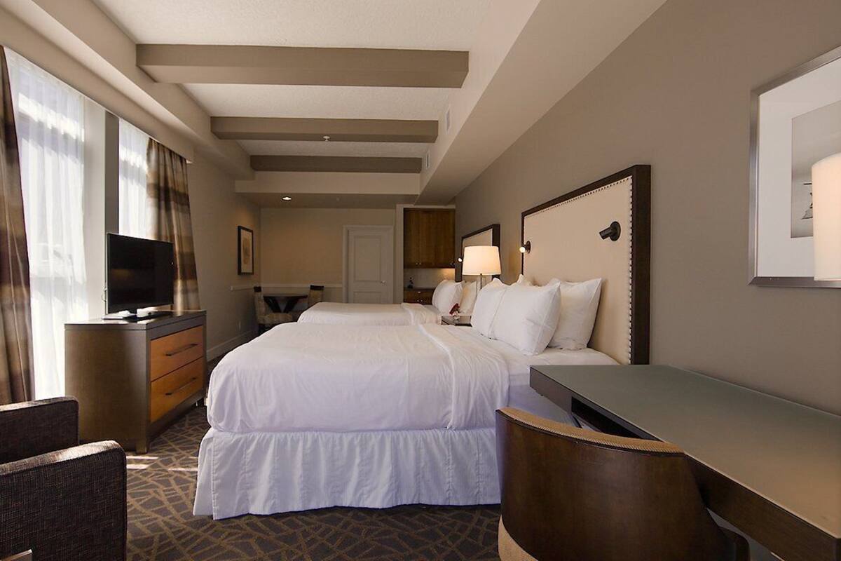 A hotel room with a large bed, a desk, a chair, a TV, and a window with curtains.