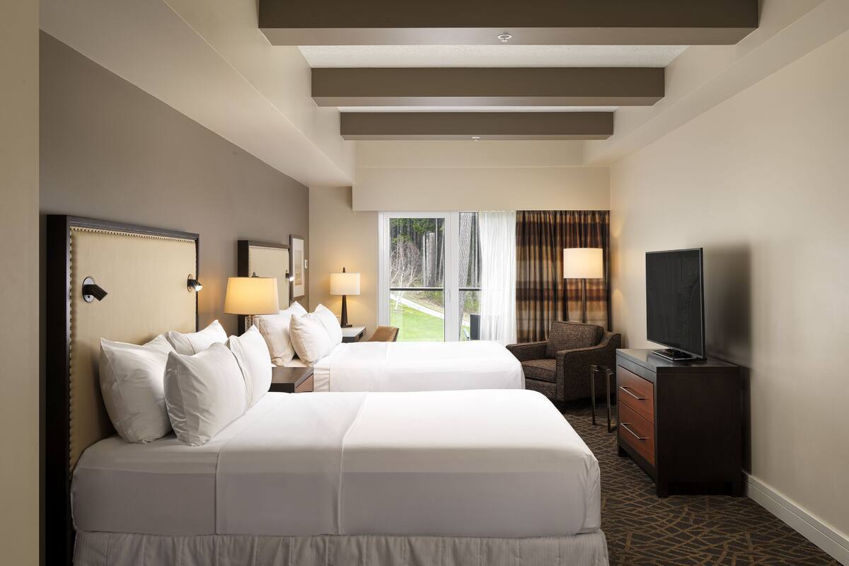A hotel room with two beds, a TV, a desk, and a chair.