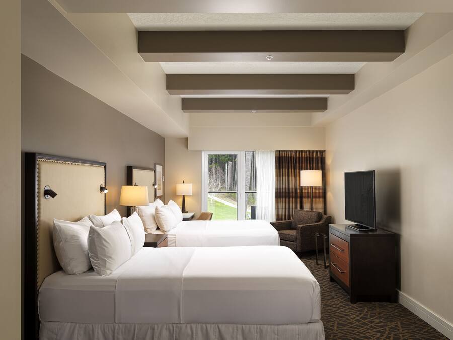 A hotel room with two beds, a TV, a desk, and a chair.