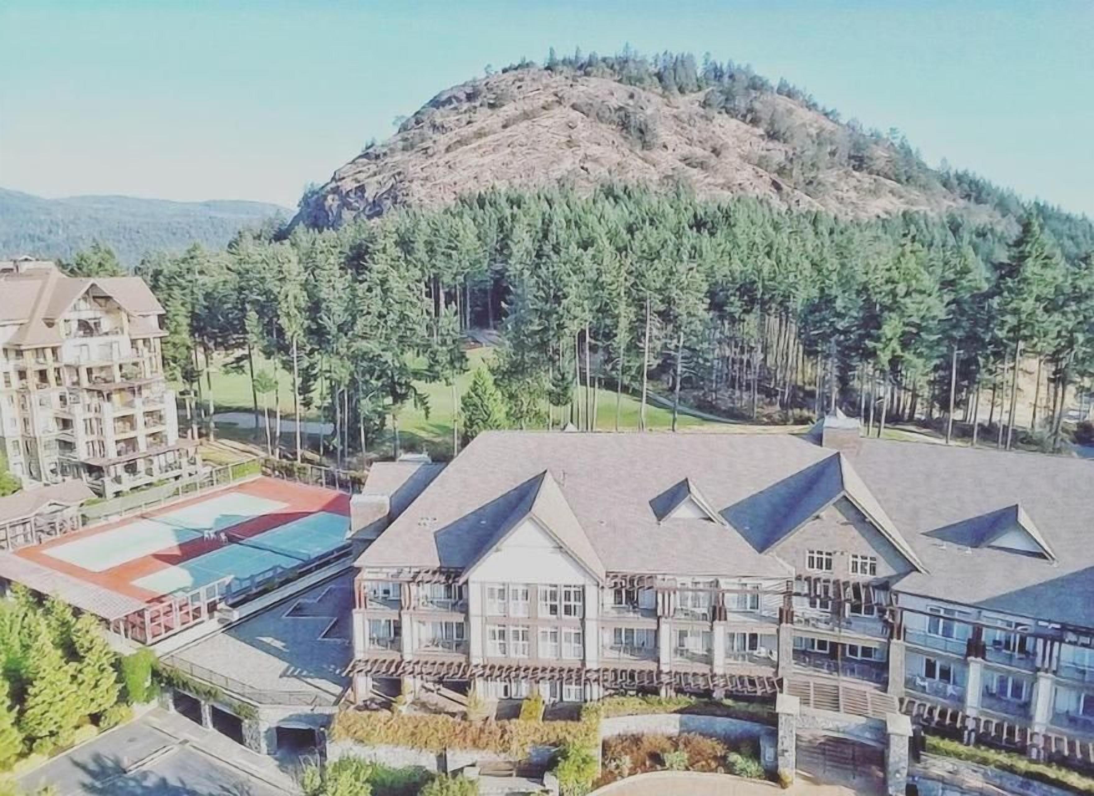 Um hotel com vários edifícios, piscina e uma colina arborizada ao fundo.