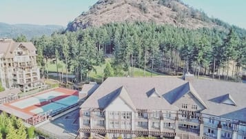 Um hotel com vários edifícios, piscina e uma colina arborizada ao fundo.