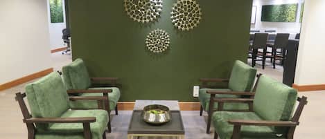 Eine Lobby mit grünen Sitzmöglichkeiten, einem zentralen Couchtisch und dekorativen Wandbildern.