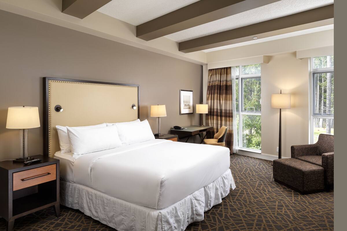 A hotel room with a large bed, two bedside tables, a desk, a chair, and a window with curtains.