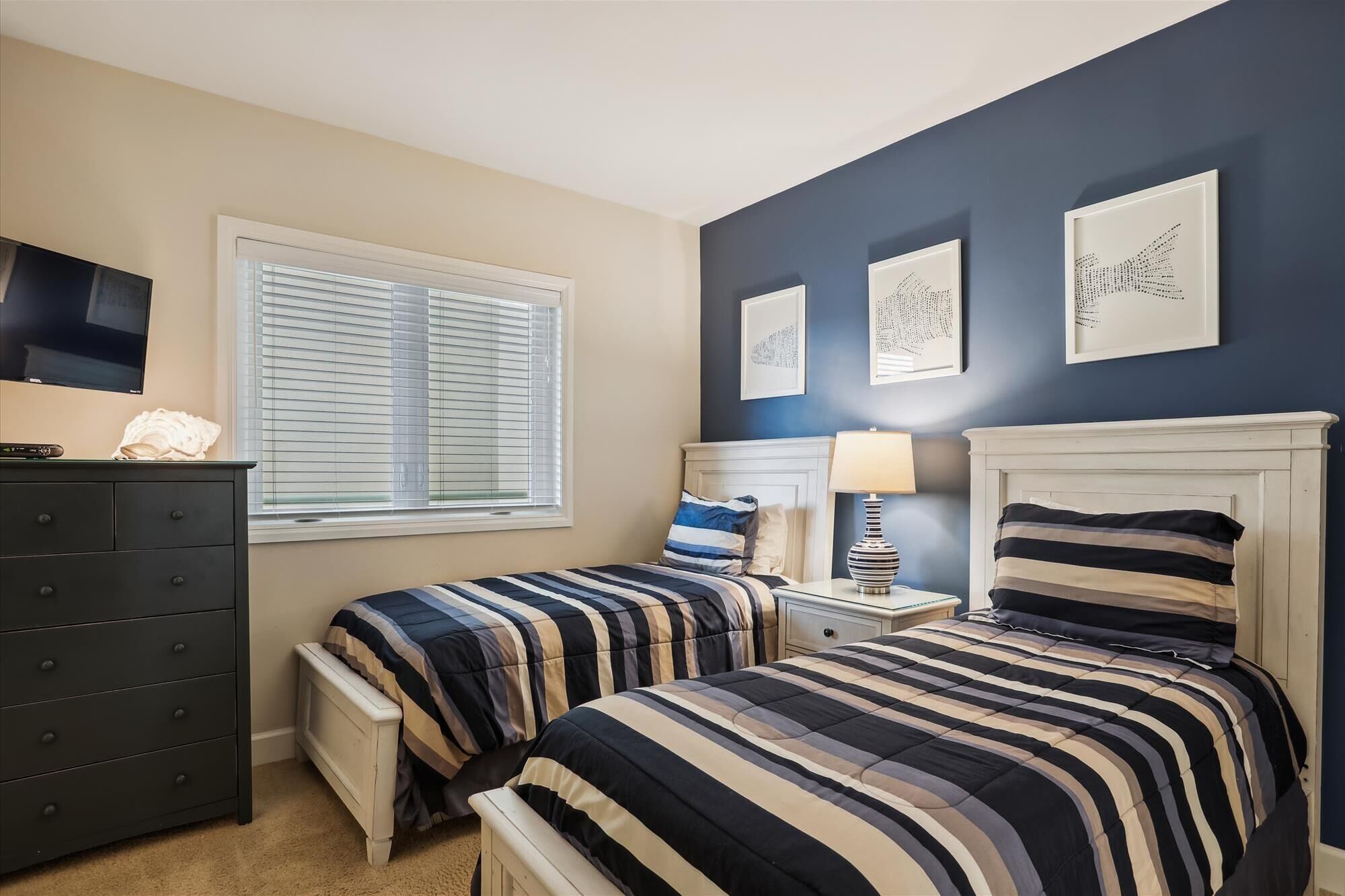 A bedroom with two beds, a dresser, a TV, and artwork on the wall.
