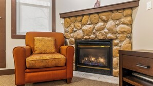 A living room with a stone fireplace, a sofa with a patterned cushion, and a wooden cabinet. - Time for a Getaway? Pool and A/C (Fernie)