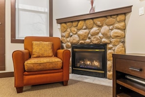 A living room with a stone fireplace, a sofa with a patterned cushion, and a wooden cabinet.