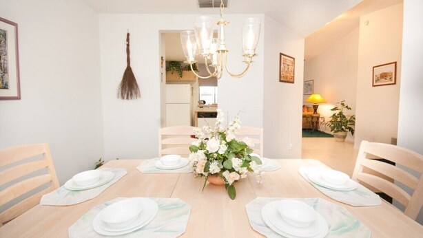 Uma sala de jantar com uma mesa de madeira posta para quatro pessoas, um candelabro e um vaso de flores.