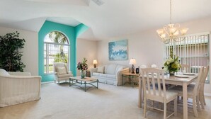 A spacious living room with a teal accent wall, a dining area with a chandelier, and a large window providing natural light. - Oak Island Retreat (Kissimmee)