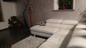 A modern living room with a white sectional sofa, a decorative tree, and a small window with a plant. - Villa la Tour Deluxe (Nus)