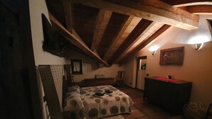 A dimly lit attic bedroom with a wooden ceiling, a bed with a patterned bedspread, a dresser, and a small chair. - Villa la Tour Deluxe (Nus)