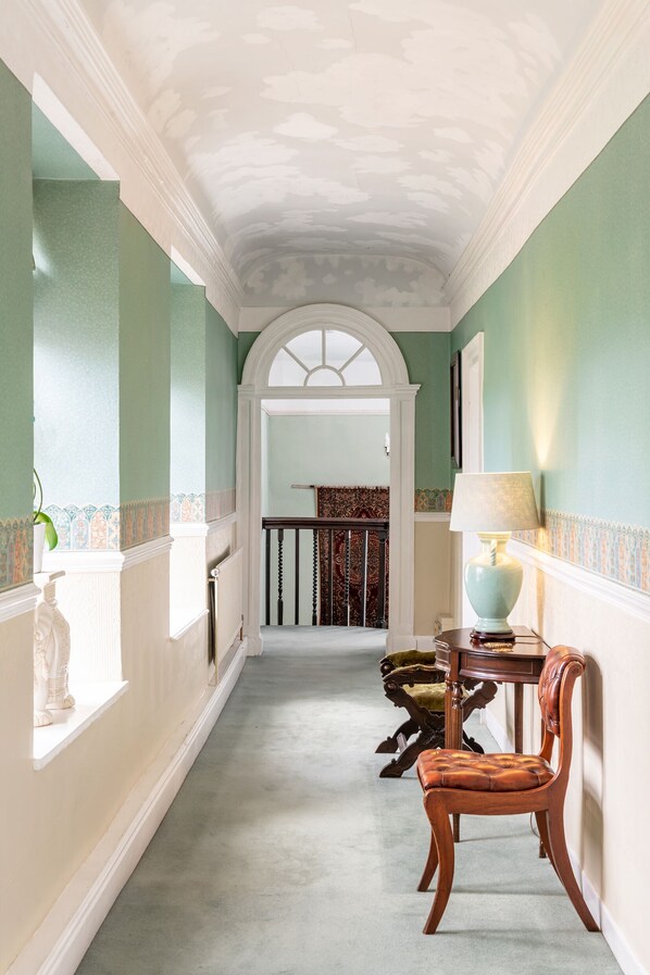 A hallway with a wooden chair, a table with a lamp, and a staircase leading to a room. - The Old Parsonage (Bristol)