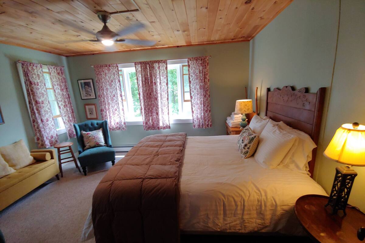 A bedroom with a bed, a nightstand, a lamp, a chair, and a window with curtains.
