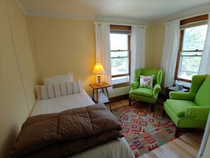 A room with a bed, two green armchairs, a small table with a lamp, and a window with curtains. - Keene Valley Lodge (Keene Valley)