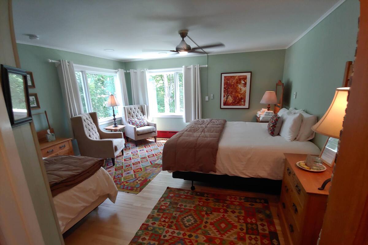 A bedroom with a bed, two chairs, a desk, a lamp, and a window with curtains.