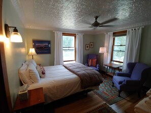 A bedroom with a bed, two chairs, a nightstand, a lamp, and a ceiling fan. - Keene Valley Lodge (Keene Valley)