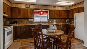 A kitchen with wooden cabinets, a microwave, a refrigerator, and a dining table with chairs. - Shoshone Canyon House- Great Location, Canyon Views (Cody)