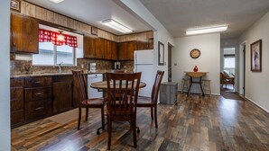 A kitchen with wooden cabinets, a dining table with chairs, a refrigerator, and a clock on the wall. - Shoshone Canyon House- Great Location, Canyon Views (Cody)