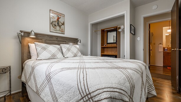 A neatly made bed with a quilted bedspread, a wooden headboard, and a wall-mounted lamp. - Shoshone Canyon House- Great Location, Canyon Views (Cody)