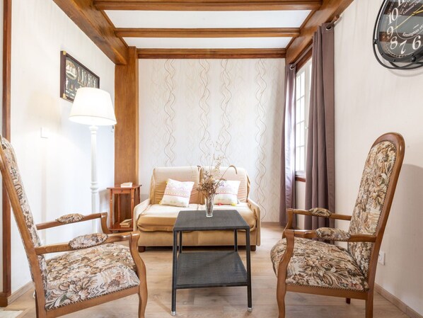 A cozy living room with a sofa, two armchairs, a small table, and a wall clock.