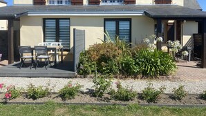 A two-story house with a patio area, a dining table with chairs, and a garden with various plants and flowers. - Cosy apartment in villa for 4 guests with WIFI, TV, terrace, pets allowed and panoramic view (Barneville-carteret)