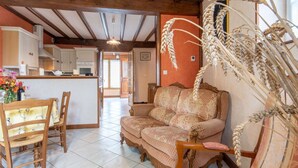 A cozy living room with a sofa, chairs, and a dining table. A kitchen is visible in the background. - Cosy apartment in villa for 4 guests with WIFI, TV, terrace, pets allowed and panoramic view (Barneville-carteret)