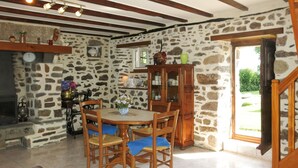 A stone-walled dining area with a wooden table and chairs, a cabinet with glass doors, and a view through a glass door to the outside.