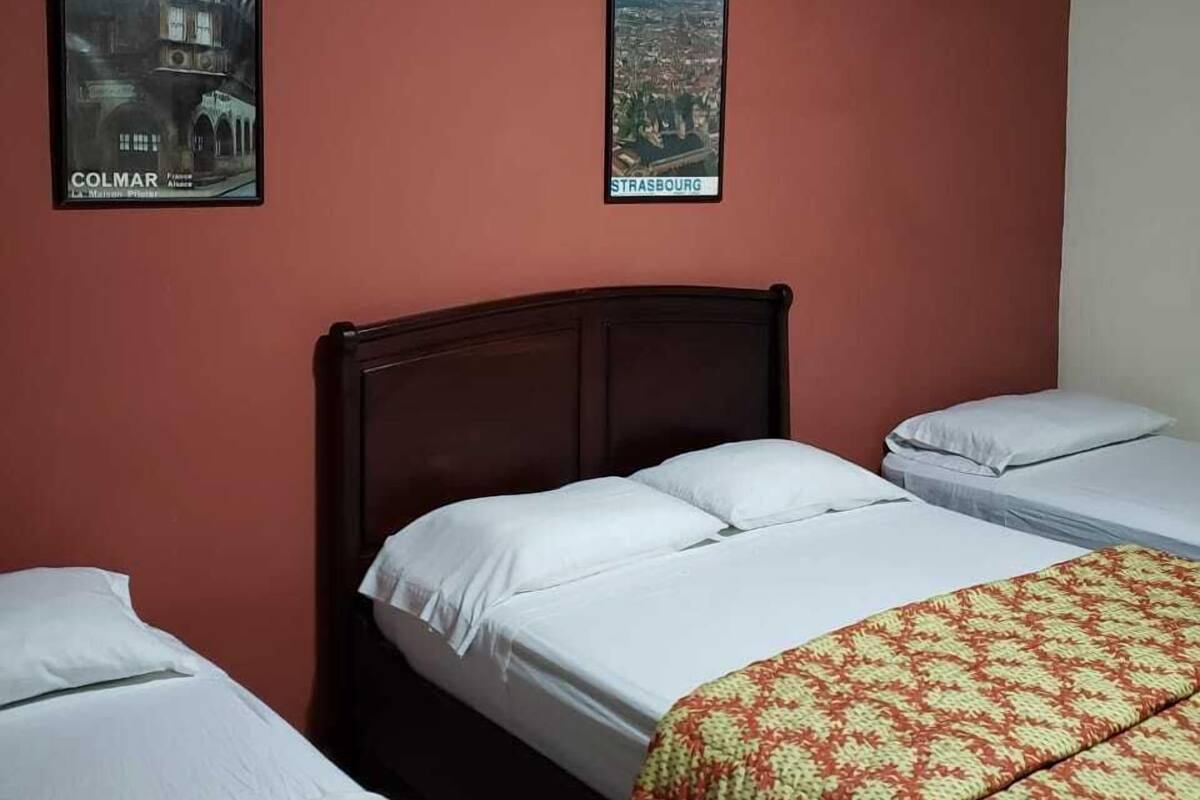 A room with two beds, a wooden headboard, and two framed pictures on the wall.