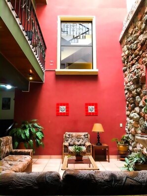 A red-walled room with a window, a staircase, a sofa, a table, and a lamp. - Hotel Alsacia (Tegucigalpa)
