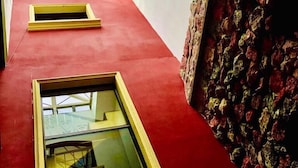 A room with a red carpet, a large window with a grid pattern, and a stone-patterned wall. - Hotel Alsacia (Tegucigalpa)