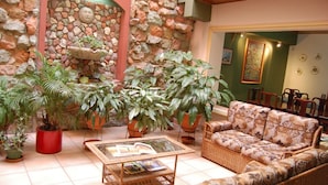 A cozy living area with a stone wall, potted plants, a wicker sofa, and a glass coffee table. - Hotel Alsacia (Tegucigalpa)