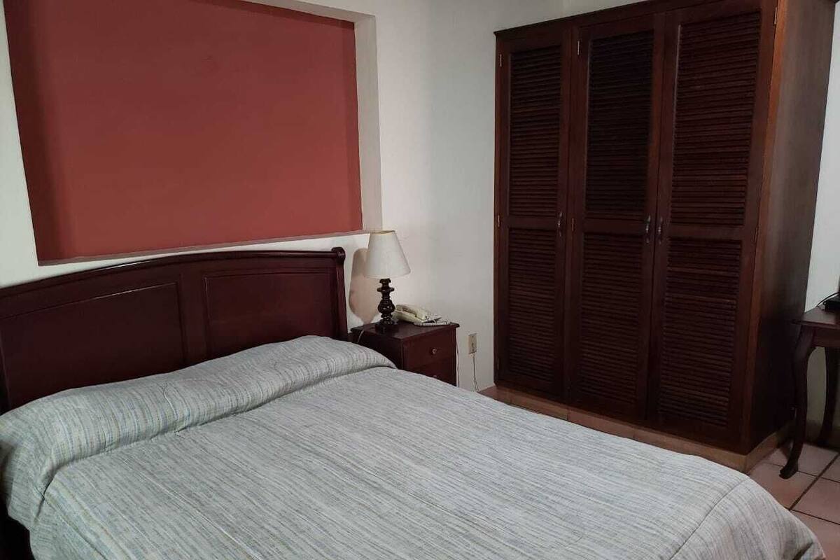 A bedroom with a bed, a nightstand, a lamp, and a wardrobe.