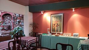 A restaurant with checkered tablecloths, wooden chairs, a stone wall, and a painting on the wall. - Hotel Alsacia (Tegucigalpa)
