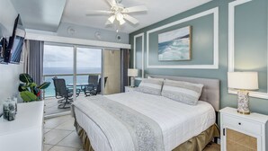 Ein Hotelzimmer mit einem großen Bett, einem Deckenventilator, Blick auf den Ozean und einem Balkon mit Stuhl und Tisch.