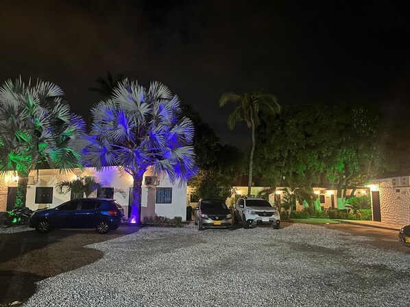 Un bâtiment avec une allée gravillonnée, des voitures garées et des palmiers.