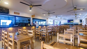 Un restaurant avec des tables et des chaises en bois, des ventilateurs de plafond et un coin bar.