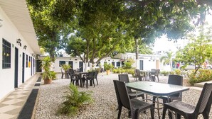 Un patio al aire libre con mesas y sillas, rodeado de edificios blancos y follaje.