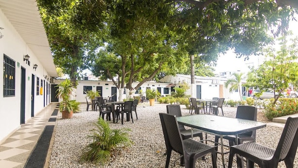 Un espace extérieur aménagé en terrasse, avec des tables et des chaises, entouré de bâtiments blancs et de verdure.