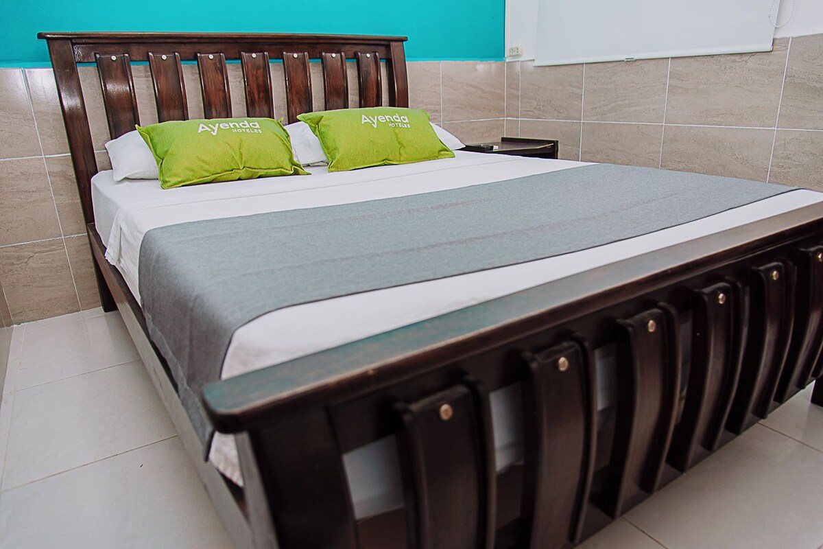 Ein Bett mit Holzrahmen, grünen Kissen und einer grauen Bettdecke in einem Zimmer mit gefliesten Wänden.