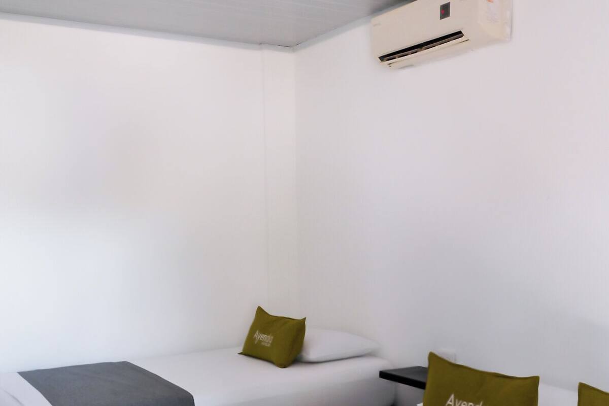 Een hotelkamer met twee bedden, elk met een grijs en wit dekbed, en een eenpersoonsbed met een grijs en wit dekbed. Daarboven bevinden zich wandmontage airconditioners.