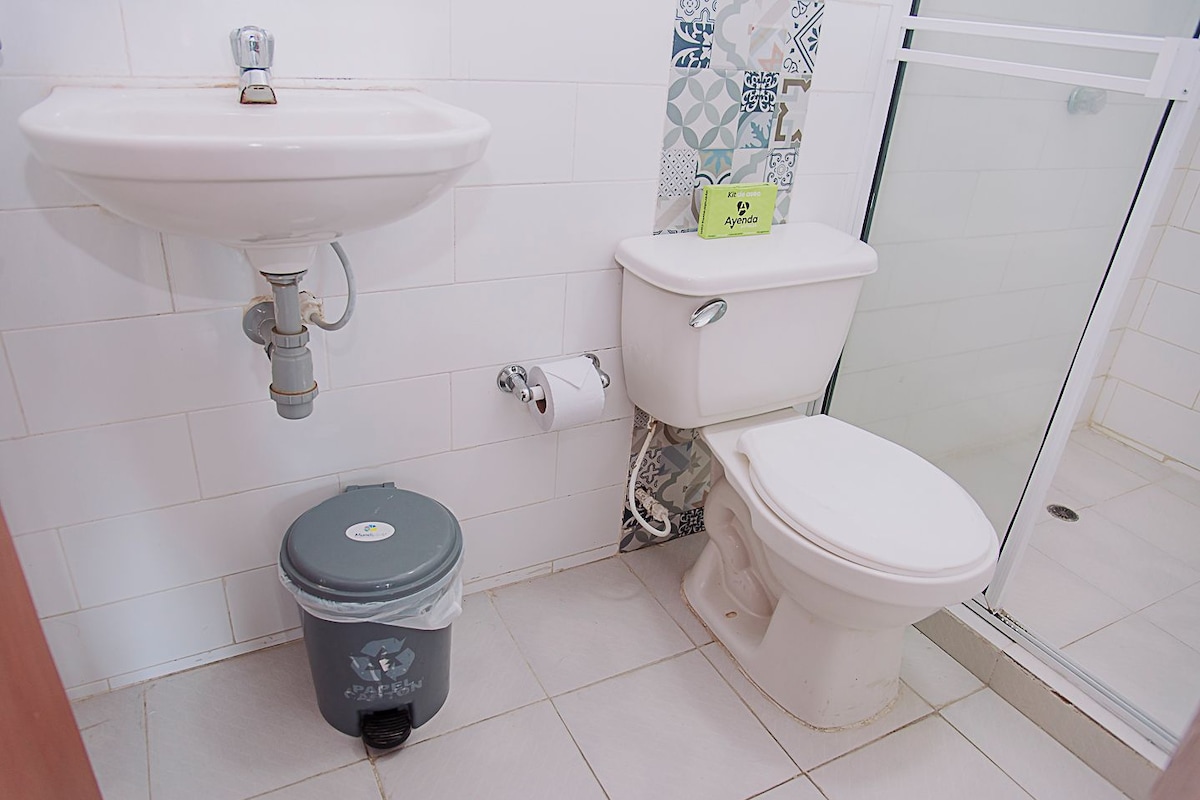 Une salle de bain avec un lavabo, des toilettes et une douche, le tout de couleur blanche.
