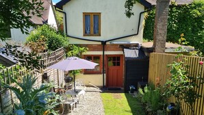 Een huis met een tuin, een terras met stoelen en een parasol, een houten omheining en een rode deur.