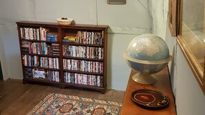 Een kamer met een houten boekenkast vol boeken, een wereldbol op een houten standaard, en een kamerbreed tapijt op de vloer.