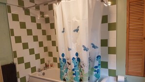 Een badkamer met een bad, toilet en een douchegordijn met een bloemenmotief.