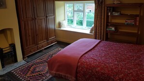 Een slaapkamer met een groot bed, een raam met gordijnen, een houten garderobe en een boekenkast.